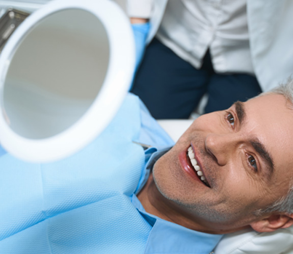 Man smiling at reflection in handheld mirror