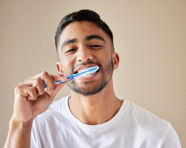 Man smiling while brushing his teeth