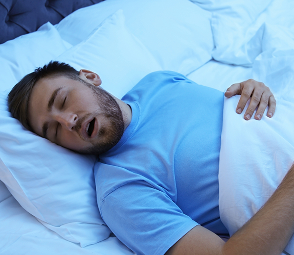 Man in blue shirt lying in bed and snoring