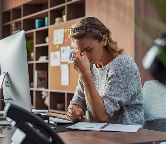 Woman in grey shirt sitting at desk looking tired