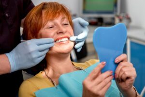 Woman smiling into mirror in dentist's chair. 