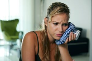 Woman holding cold compress to jaw in pain.